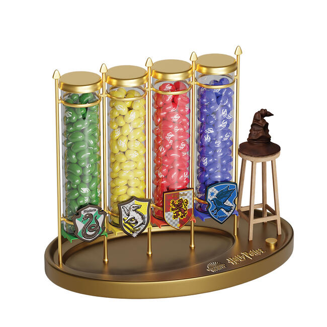 Un distributeur de Jelly Belly Harry Potter avec 4 compartiments contenant 4 sortes de Jelly Belly différents : vert, jaune, rouge et bleu. A sa droite le Choixpeau magique sur un tabouret, le tout sur un fond blanc