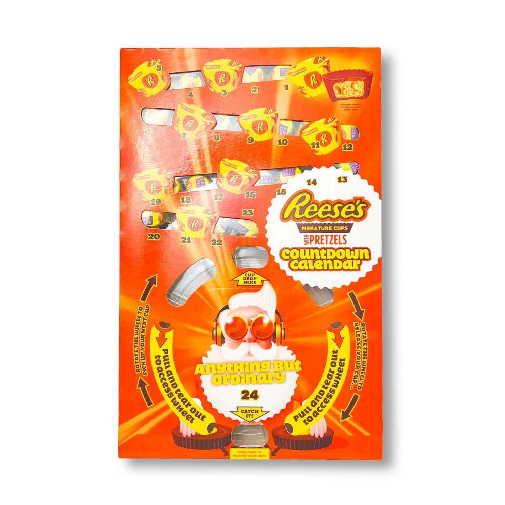 Un emballage orange sur fond blanc avec sur le bas le visage d’un père Noël avec de grosses lunettes de soleil et un casque de musique. Vers le haut il y a des zones transparentes permettant de voir les Reese’s Miniature Cups
