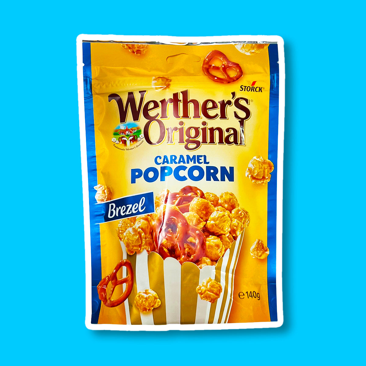 Un emballage de couleur orange et aux extrémités bleues, avec un paquet de popcorn au caramel et bretzel. Sur le côté gauche, il y une étiquette bleu « Brezel » le tout sur fond bleu