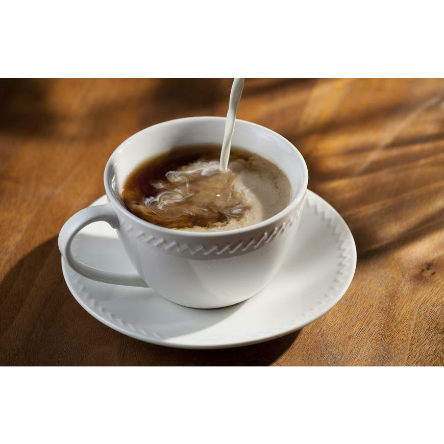 Une tasse blanche de café sur une assiette blanche avec du lait qui tombe, le tout sur une table en bois