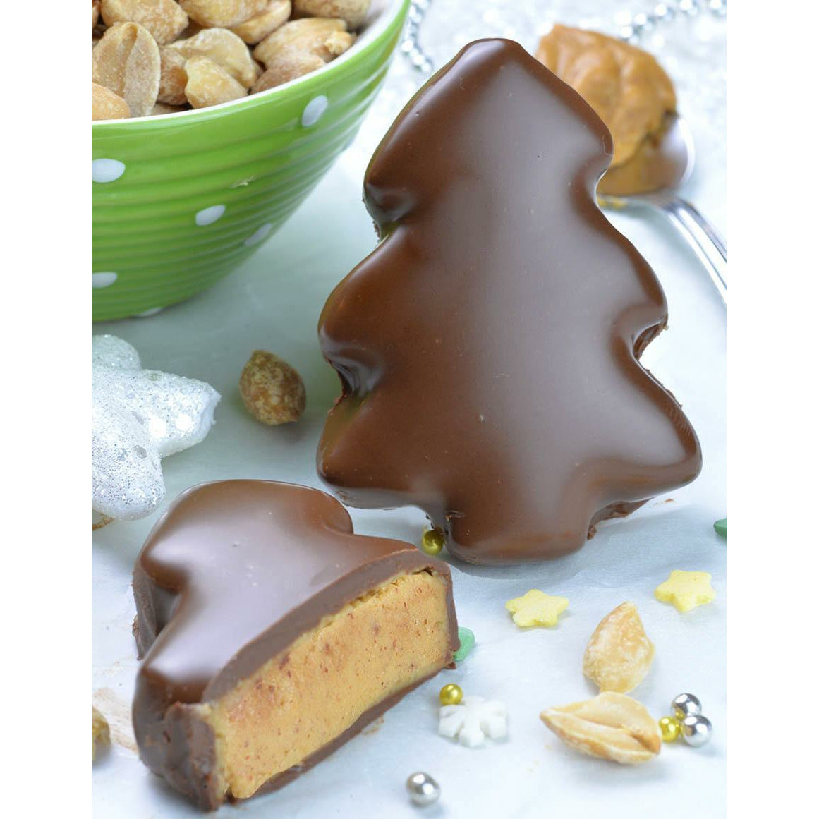 Deux Reese’s Peanut Butter Milk Chocolate Tree sur une nappe blanc dont celui de gauche qui est coupé en 2. Sur le coté gauche, il y a un bol vert rempli de cacahuètes salées