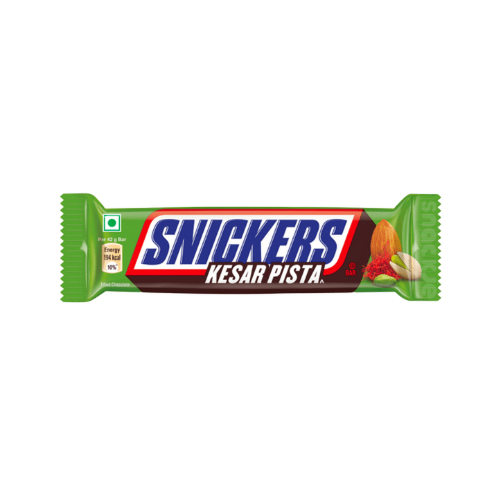 Un emballage vert sur fond blanc avec au centre écrit « Snickers » en bleu et sur le côté droit il y a une amende, une pistache et une poudre rouge