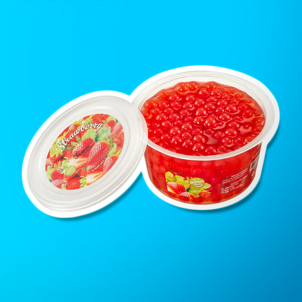Une boite sur fond bleu remplie de perles rouges et à gauche le couvercle avec plusieurs fraises