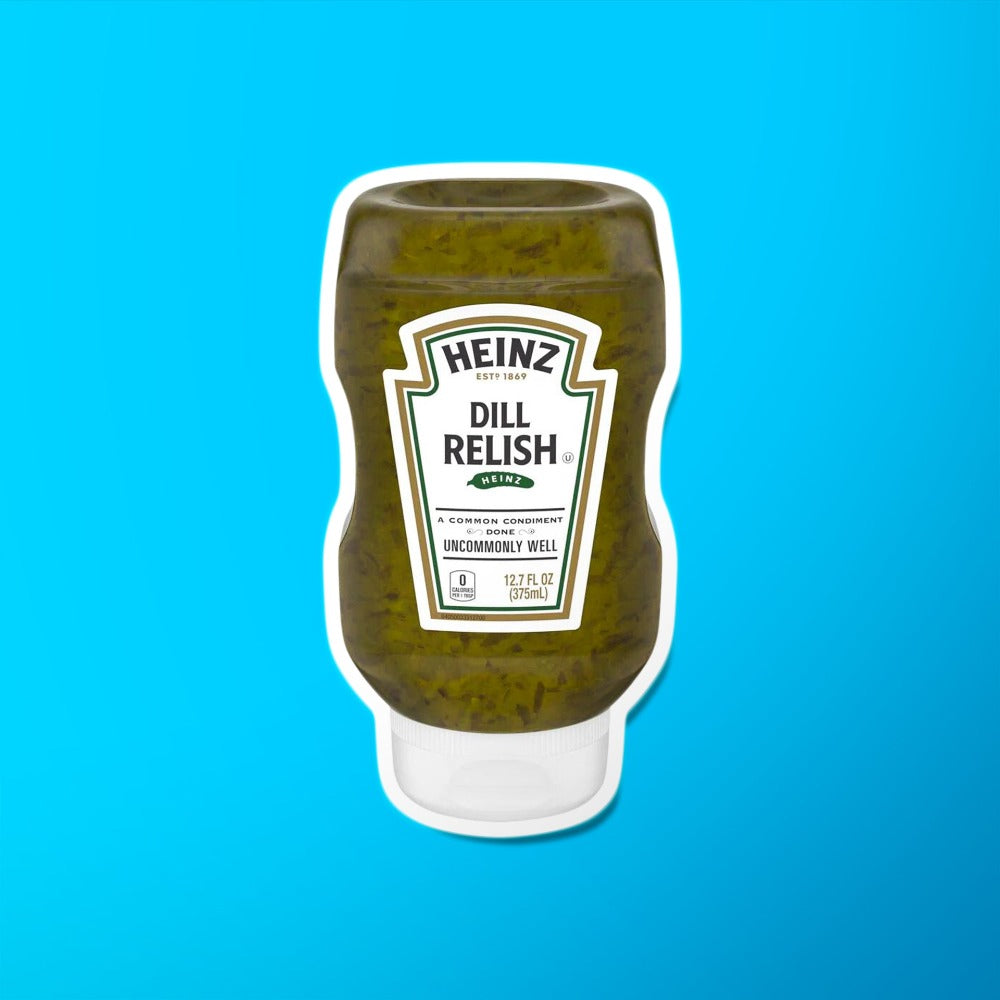 Une bouteille transparente d’une sauce verte avec des morceaux vert foncé, un capuchon blanc et une étiquette blanche au centre. Le tout sur fond bleu