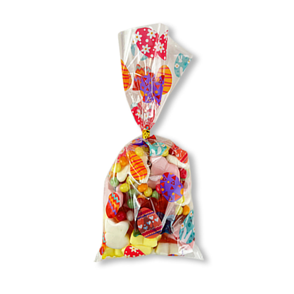 Un emballage transparent avec des motifs d’oeufs de Pâques colorés rempli de diverses bonbons, le tout sur fond blanc