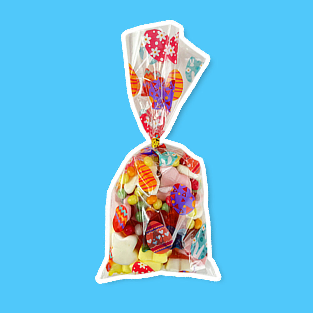 Un emballage transparent avec des motifs d’oeufs de Pâques colorés rempli de diverses bonbons, le tout sur fond bleu