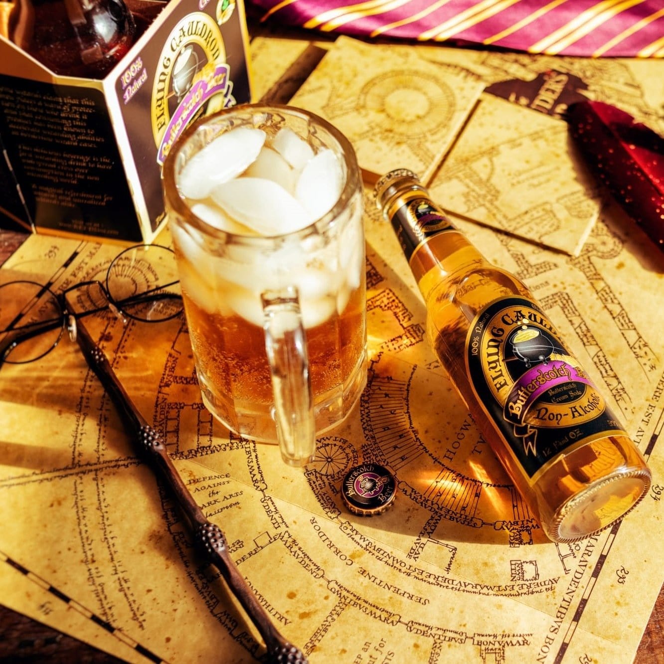 Une baguette magique, des lunettes noires, une choppe de bière et de glaçons et une bouteille en verre d’une boisson brune sur une carte beige 