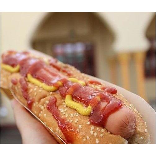 Une main qui tient un hot-dog avec sur le dessus une sauce rouge et une sauce jaune