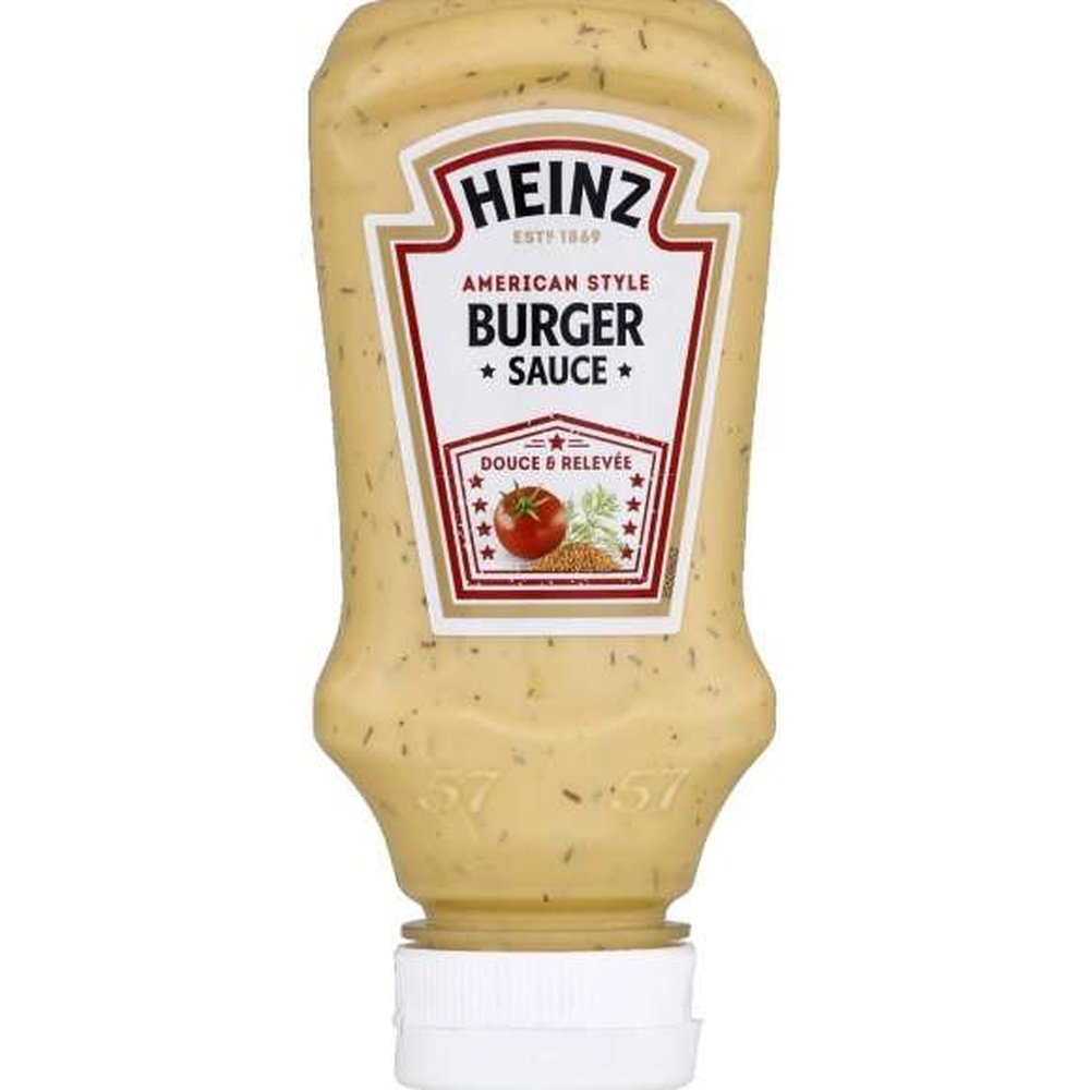 Une bouteille transparente d’une sauce beige, un capuchon blanc et une étiquette blanche au centre avec une tomate et des épices. Le tout sur fond blanc