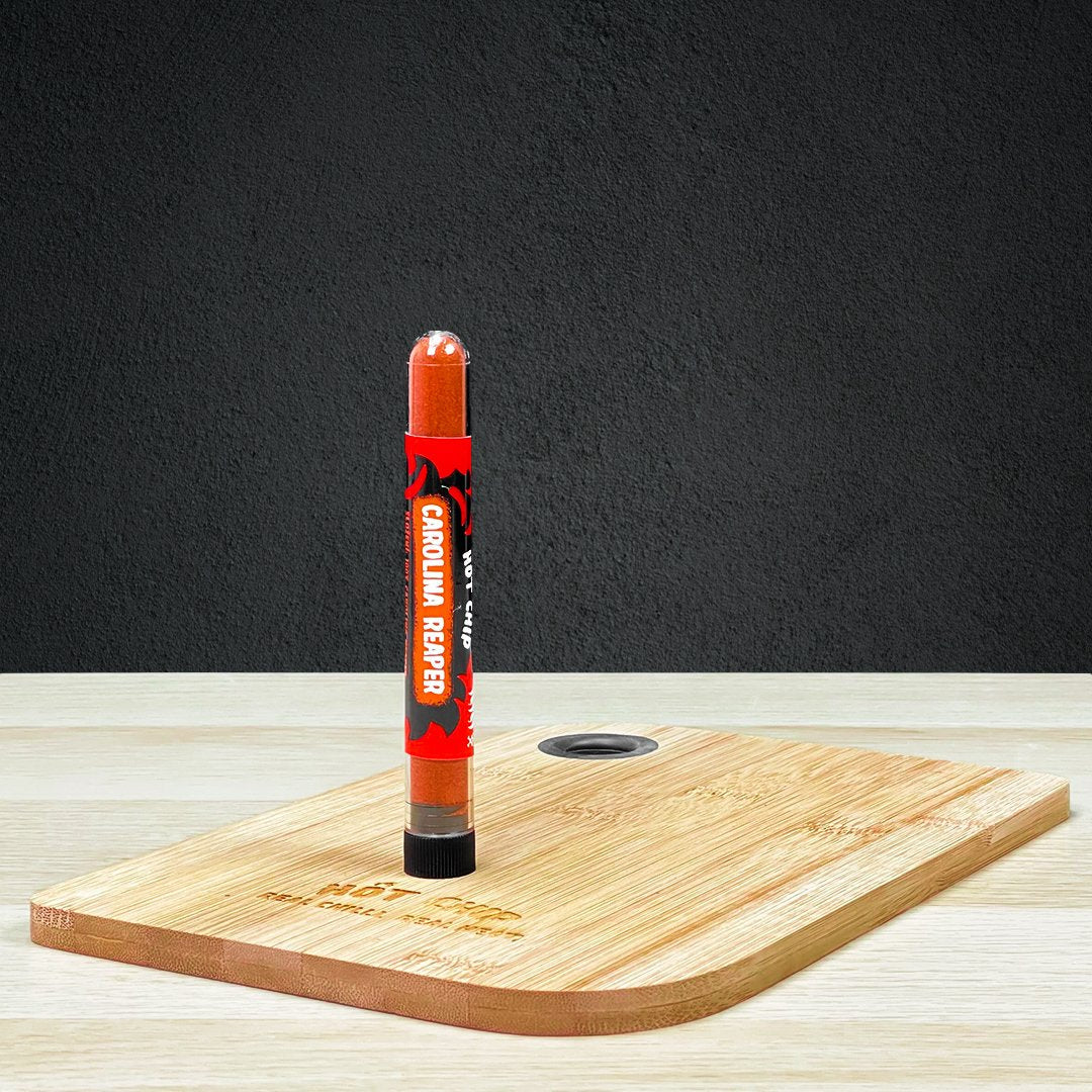 Une planche en bois sur une table en bois avec au-dessus une fiole en verre avec des épices oranges. Le tout devant un mur noir