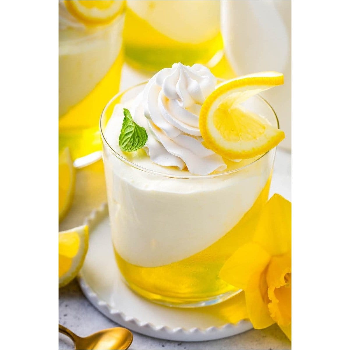 Un verre transparent avec une couche de gelée jaune séparé obliquement d’une couche de crème et au-dessus de la chantilly et une tranche de citron 
