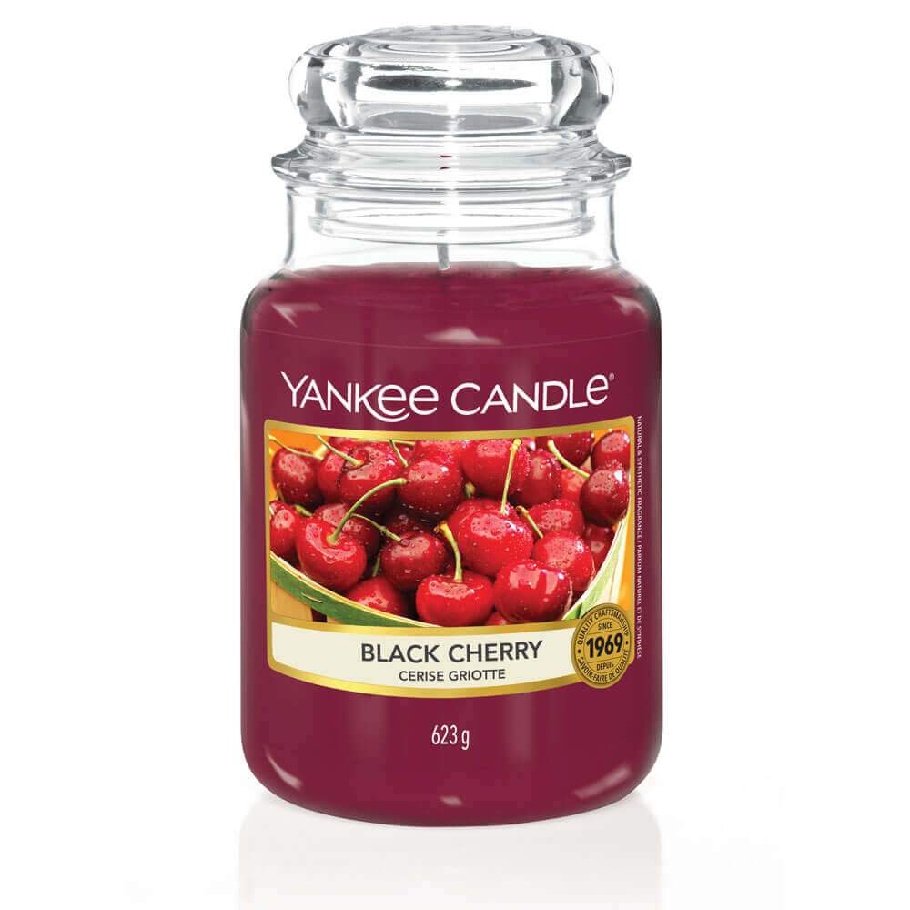 Un emballage sur fond blanc avec une bougie rouge bordeaux dans un bocal en verre, un capuchon en verre et une étiquette avec un panier de cerises rouges humides