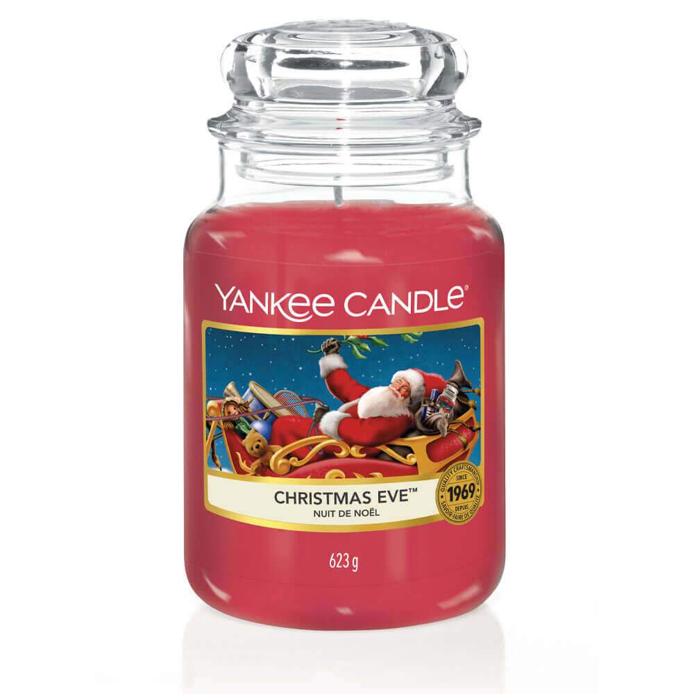 Un emballage sur fond blanc avec une bougie rouge dans un bocal en verre, un capuchon en verre et une étiquette avec le Père Noel sur son traineau rouge et en or
